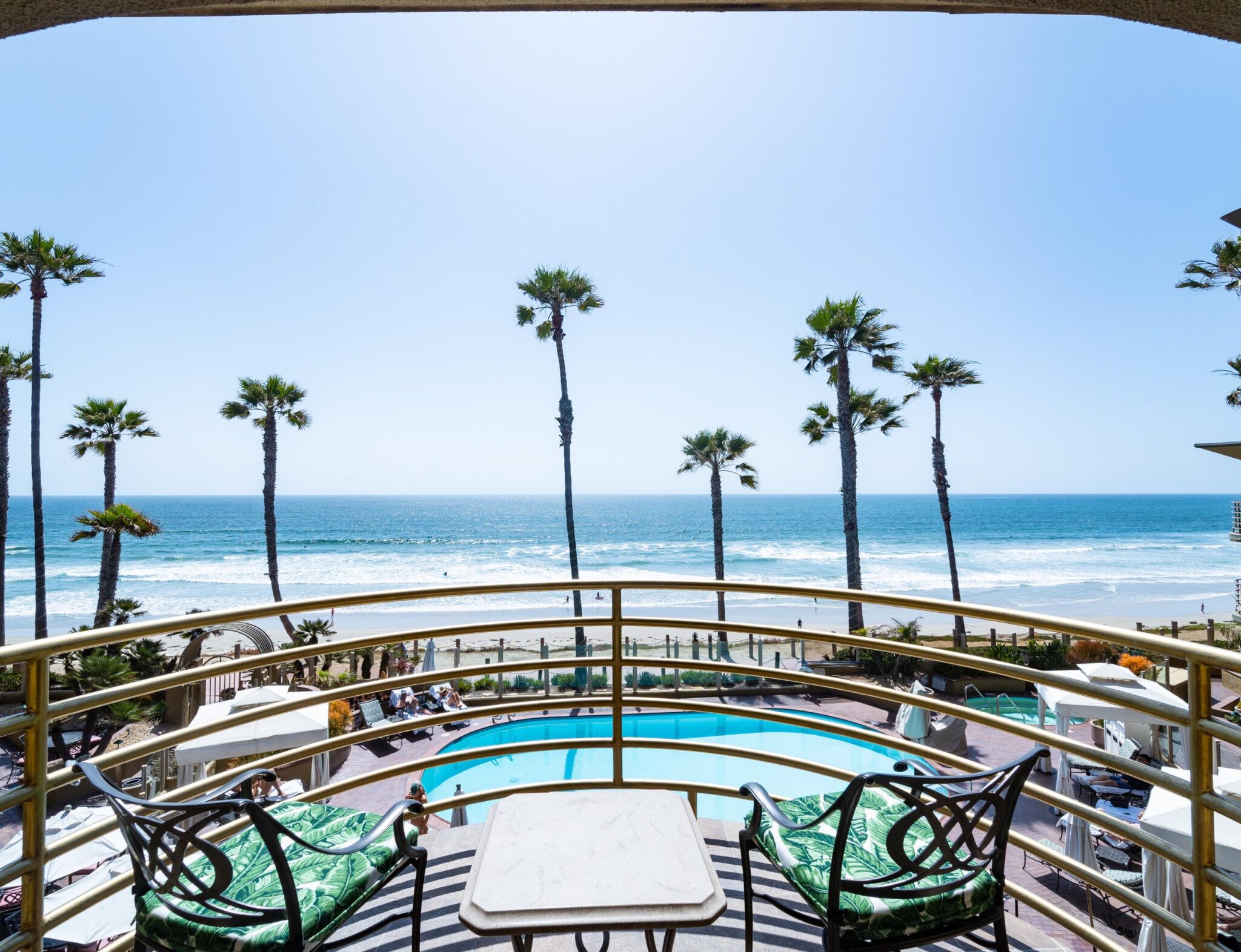 Balcony with a view of tall trees, pool, and pacific beach